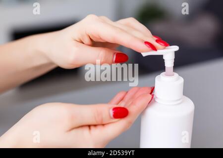 Donna premere sul dispenser e strizzare il gel di sapone morbido sul palmo, colpo di closeup su fondo piatto. Sapone liquido trasparente utilizzato per il lavaggio delle mani Foto Stock