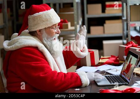 Babbo Natale videochiamata su laptop saluto bambino sedersi al tavolo da officina. Foto Stock