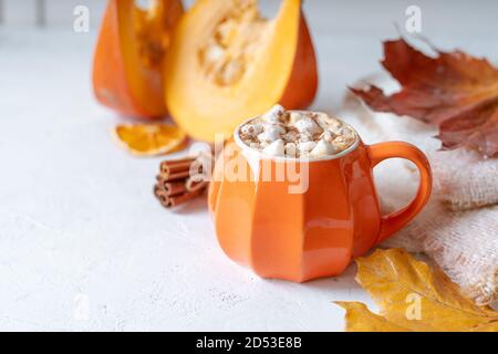 Composizione con tazza di caffè in stile zucca arancione con marshmallows e decorazioni a tema autunnale, foglie cadute, maglione accogliente su sfondo bianco. Foto Stock