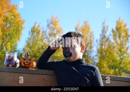 ragazzo con trucco nero per halloween, zombie. Spaventoso ragazzo sorridente indossando il trucco del cranio per Halloween lanterna di zucca, dolci Foto Stock