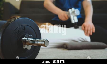 Terapista massaggiando la schiena della donna con un dispositivo di percussione massaggiante a casa sua. Foto Stock