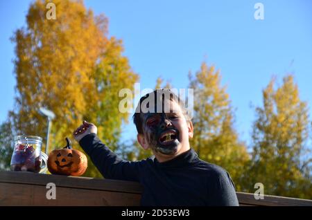 ragazzo con trucco nero per halloween, zombie. Spaventoso ragazzo sorridente indossando il trucco del cranio per Halloween lanterna di zucca, dolci Foto Stock