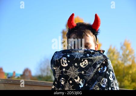 bambino divertente in costume halloween diavolo con corna e tridente su un ragazzo di sfondo di legno scuro con trucco nero per halloween, zombie Foto Stock