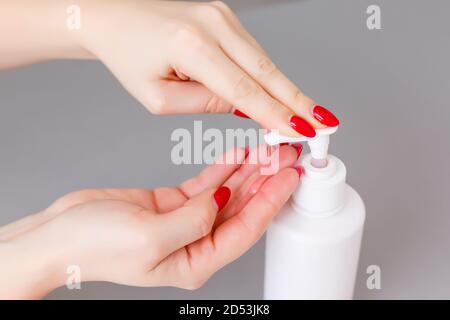 Donna premere sul dispenser e strizzare il gel di sapone morbido sul palmo, colpo di closeup su fondo piatto. Sapone liquido trasparente utilizzato per il lavaggio delle mani Foto Stock