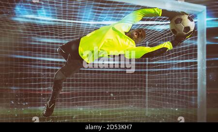Il portiere di calcio, in uniforme fluorescente, fa un salvataggio ed evita un gol durante una partita notturna Foto Stock