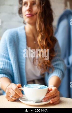 Donna felice non messa a fuoco con lunghi capelli ondulati in maglione caldo per tenere una tazza di latte blu caldo Foto Stock