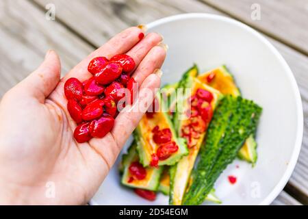 Closeup di mano che tiene rosso melone amaro semi di verdure rivestimento che ha un sapore e un aspetto simile a peperoni rossi arrostiti con sfondo della piastra Foto Stock