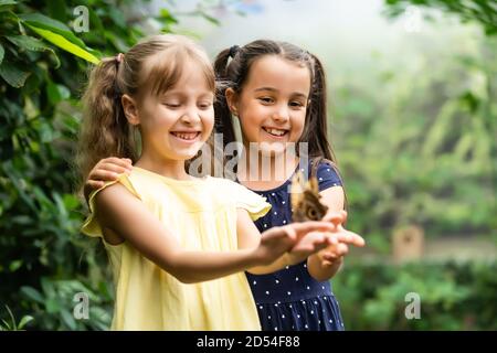 Due piccole sorelle che tengono una farfalla nelle loro mani. Bambini che esplorano la natura. Vacanza in famiglia con i bambini in estate. Foto Stock