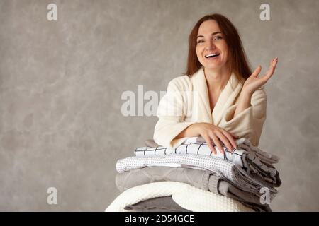 Giovane donna con bel sorriso in caldo beige accappatoio è appoggiarsi alla risma di fogli piegati Foto Stock