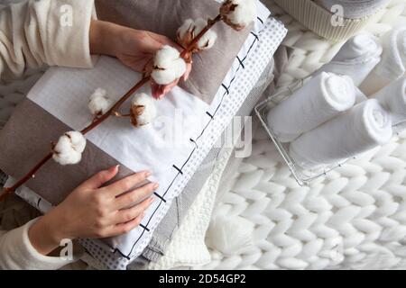 Donna mano che tiene un ramo di cotone con pila di piegato biancheria vicino asciugamani arrotolati in maglia cesto Foto Stock