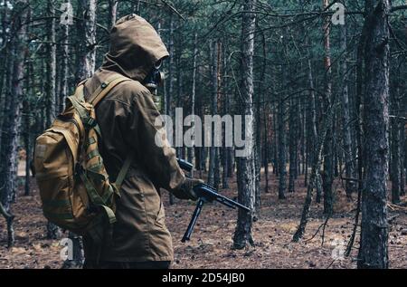 Foto di un soldato di stalker di guerra nucleare in piedi e in posa in maschera di gas sovietica, zaino con fucile in legno vista posteriore. Foto Stock