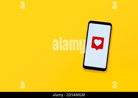 Vista dall'alto del telefono cellulare con emoticon del cuore. Design minimalista. Schermo bianco e sfondo giallo, spazio per la copia. Concetto di social network. Foto Stock