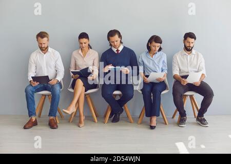 I cercatori di lavoro con i resumes nelle mani che attendono l'intervista di lavoro seduta su sedie in fila Foto Stock