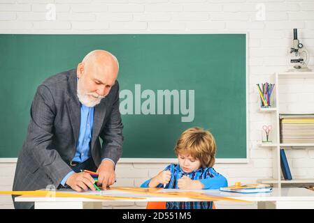 Insegnante di scuola elementare che dà sostegno alla pupilla femminile in classe. Lezione di bambino a scuola con insegnante senior. Foto Stock