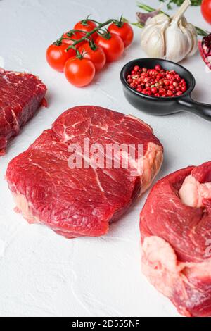 Tagli di manzo rullo occhio di Chuck, lama superiore, bistecca di groppa con vino rosso in bicchiere e bottiglia, erbe e melograno. Carne biologica. Sfondo bianco con texture Foto Stock