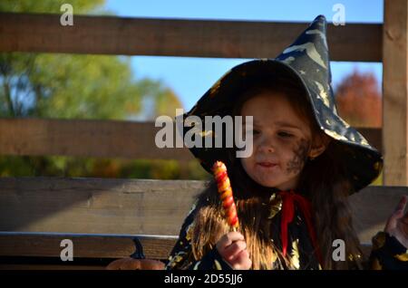 Una ragazza in una tuta strega e un cappello nero sulla testa con Halloween nero make-up, zombie mangiare dolci jelly vermi a una celebrazione di Halloween Foto Stock