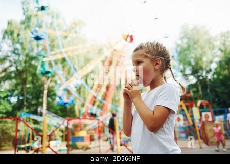 Carino bambina mangia gelato nel parco a. diurno vicino alle attrazioni Foto Stock