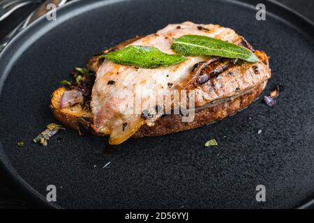 Pancetta di fegato e cipolle sul pane cotto pasto sul piatto su superficie nera Foto Stock