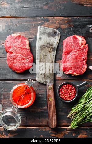 Bistecca di manzo biologica tagliata, bistecca di manzo marmorizzato crudo, con scagliatore vecchio coltello macellaio, condimento su tavolo rustico di legno scuro, vista dall'alto Foto Stock