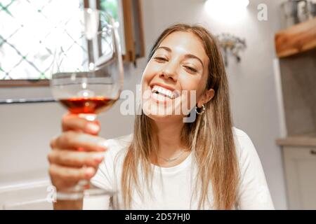 Carina giovane bionda caucasica tostatura con bicchiere di vino rosso Guardare la fotocamera a casa - nuovo telecomando normale comunicazione in conferenza via internet Foto Stock