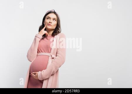 donna incinta con la fascia che tocca il viso e guarda in alto isolato su bianco Foto Stock