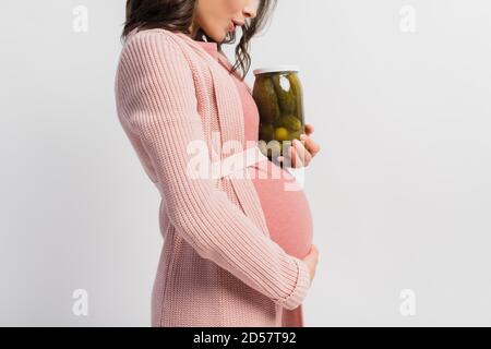 vista parziale della donna sorpresa e incinta che tiene il vaso con cetrioli decapati isolati su bianco Foto Stock