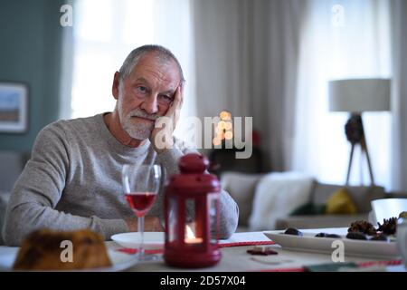 Solitario anziano con vino seduto al tavolo al chiuso a Natale, concetto di solitudine. Foto Stock