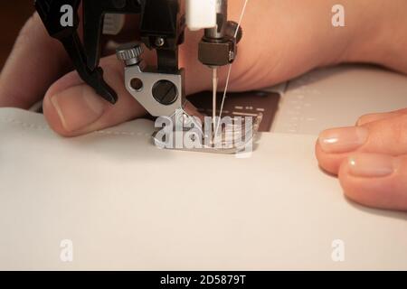 Le mani femminili sono in tessuto bianco su una macchina da cucire con posto per il testo. Atelier e concetto artigianale. Foto Stock