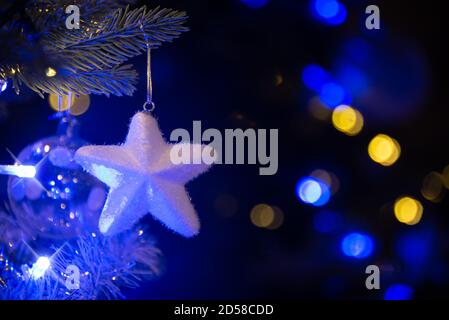 Stella bianca appesa su un albero di Natale, ornamenti di Natale di notte, luci di vacanza blu e oro Foto Stock