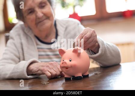 Donna anziana che mette una moneta in una banca piggy Foto Stock