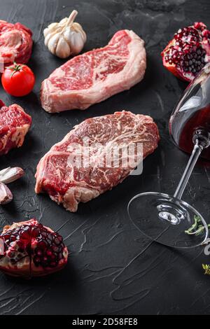 Lama superiore, tagli di bistecca di manzo, con erbe, condimento e bicchiere di vino rosso sul tavolo nero, vista laterale. Foto Stock