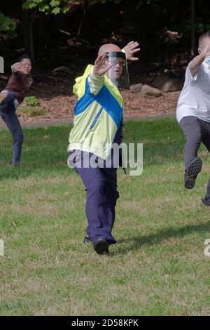 Un uomo americano asiatico che indossa uno scudo facciale ad una classe di Tai Chi in Kissena Park, Flushing, Queens, New York City. Foto Stock