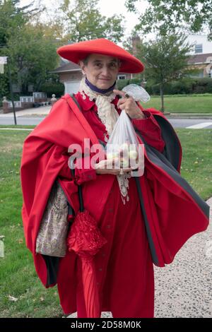 Una donna vestita quasi interamente in rosso che tiene un pacchetto di mele fresche. A Queens, New York City. Foto Stock