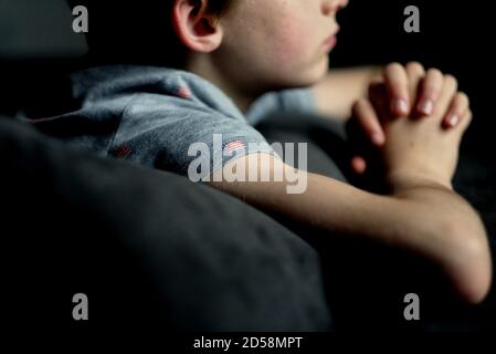 Primo piano di un ragazzo che indossa una t-shirt con bandiera americana sdraiata sul suo letto pregando Foto Stock