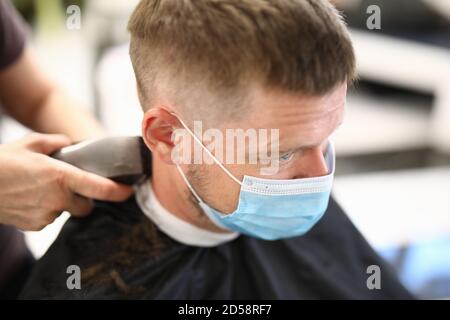 Giovane uomo in maschera protettiva sul viso fa il taglio dei capelli salone di bellezza ritratto Foto Stock