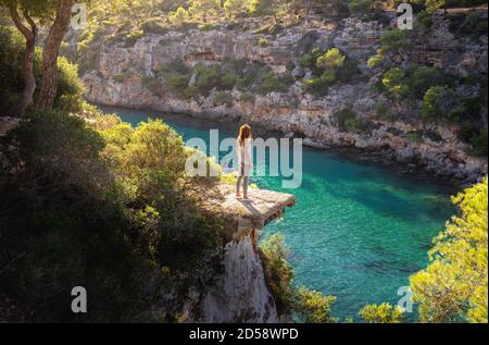 Ragazza in piedi su una sporgenza sul mare in bella luce del sole, Cala Pi, Mallorca, Spagna. Foto Stock