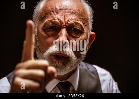 Ritratto di uomo anziano arrabbiato che minaccia. Sfondo nero. Foto Stock