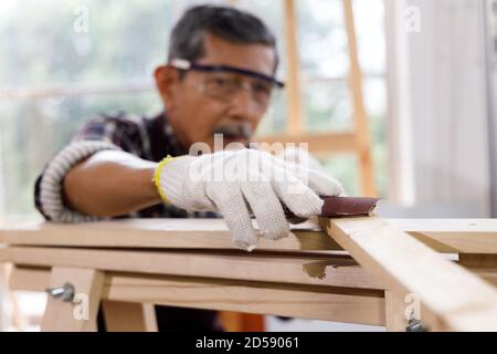 Uomo anziano lucidare legno con carta vetrata in officina di Falegnameria. Concetto di persone anziane che fanno hobby dopo il pensionamento. Foto Stock