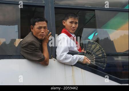 13.08.2012, Pyongyang, Corea del Nord, Asia - l'uomo e un ragazzo che indossa l'uniforme dei giovani pionieri e tiene un fan della mano guardano fuori una finestra dell'autobus. Foto Stock