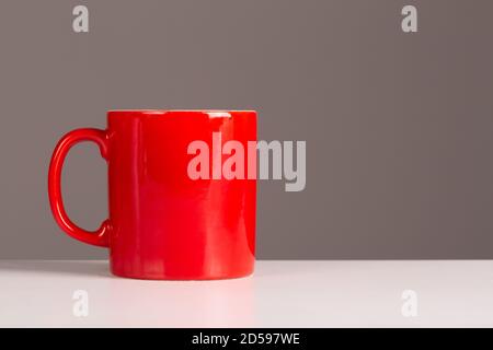 Un caffè rosso brillante o tazza di squadra su uno sfondo neutro con abbondanza di copyspace per i progettisti. Foto Stock