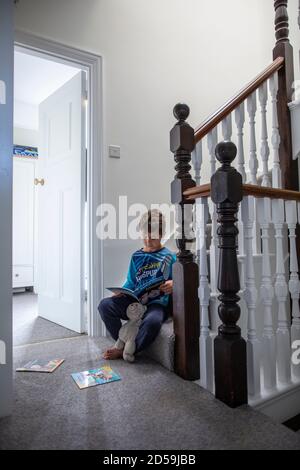 Ragazzo di sei anni che legge un libro mentre sedeva sulla sua scala residenziale, Inghilterra, Regno Unito Foto Stock