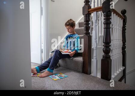 Ragazzo di sei anni che legge un libro mentre sedeva sulla sua scala residenziale, Inghilterra, Regno Unito Foto Stock