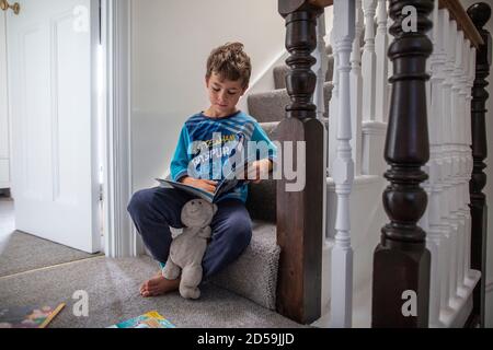 Ragazzo di sei anni che legge un libro mentre sedeva sulla sua scala residenziale, Inghilterra, Regno Unito Foto Stock