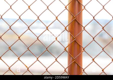 Una chiusura di una sezione di una recinzione di collegamento arrugginita della catena. Un palo di recinzione è visibile. Sito industriale in background al di fuori della profondità di campo. Foto Stock