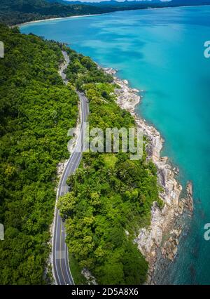 Vista aerea della strada tra palme da cocco e il grande oceano di giorno a Nakhon si Thammarat, Thailandia Foto Stock