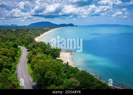 Vista aerea della strada tra palme da cocco e il grande oceano di giorno a Nakhon si Thammarat, Thailandia Foto Stock