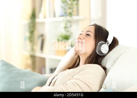 Donna soddisfatta che si rilassa seduto su un divano ascoltando musica a casa Foto Stock