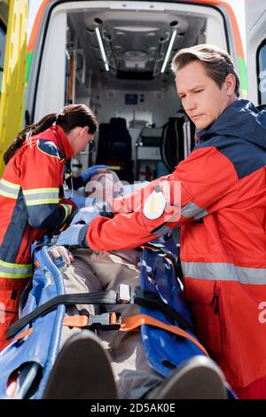 Messa a fuoco selettiva di paramedici in piedi vicino a pazienti anziani sulla barella e auto ambulanza Foto Stock