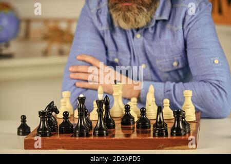 figure di scacchi su tavola di legno. Insegnante di scuola focalizzato. Pensare di attaccare e catturare pezzi di scacchi avversari. Pensare alla prossima mossa. Uomo barbuto addestramento per la competizione di scacchi. Foto Stock