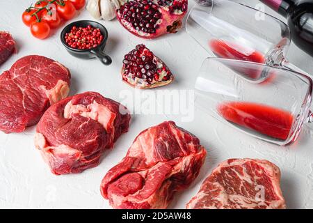 Set crudo di tagli di manzo alternativi rotolo occhio di Chuck, lama superiore, bistecca di groppa con vino rosso in bicchiere e bottiglia, erbe e melograno. Carne biologica. Bianco Foto Stock